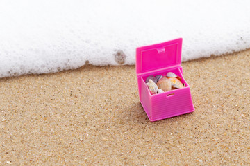 Pink toy chest with shells, on a sandy beach, with sea wave, travel and adventure concept, macro
