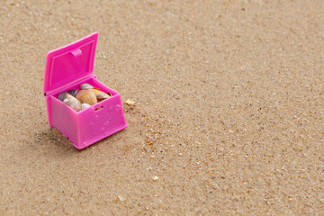 Fototapeta na wymiar pink toy chest with shells, on a sandy beach, with copy space, summer and adventure concept, macro