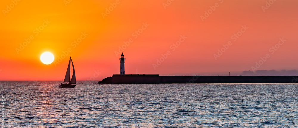 Wall mural panoramic view of ocean sunset with silhouettes of sailboat and lighthouse against the orange sky. - Wall murals