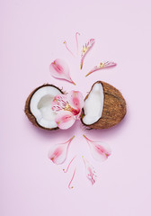 Broken coconut with tropic flowers on pink background. Top view, flat lay.
