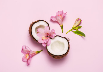 Obraz na płótnie Canvas Broken coconut with tropic flowers on pink background. Top view, flat lay.