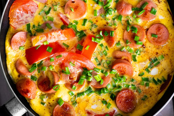 Omelette with tomato, onion and sausage on frying pan