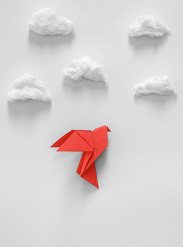 Red origami paper dove on a gray background among the white clouds.