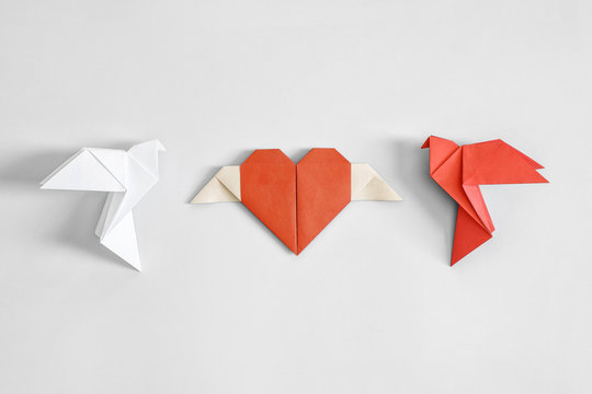 Red and white origami paper dove on a white background and a red heart.