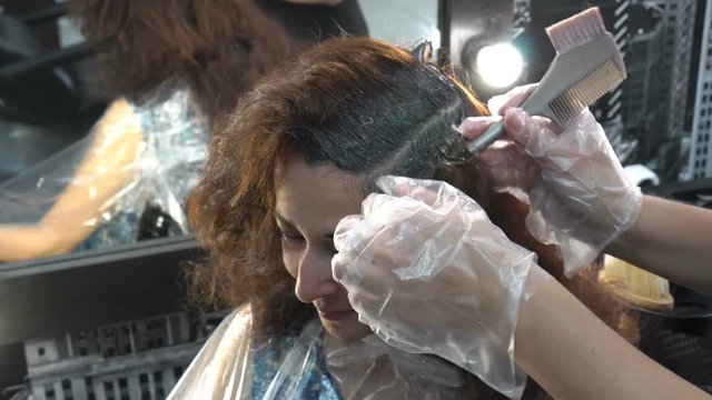 The girl's hair is dyed in a Barber shop. The Barber applied with a paint brush on her hair. Close up. 4K