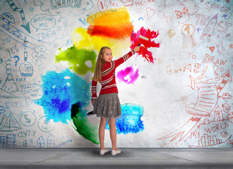 Obraz na płótnie Canvas Little girl standing in front of the wall and paints with the bright colours. Background with lots of educational icons and symbols