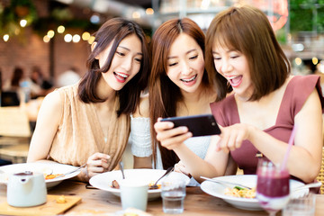 Happy friends having dinner and watching smart phone in  restaurant