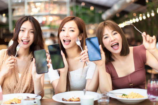 Happy Friends Having Dinner And Showing Smart Phone In  Restaurant