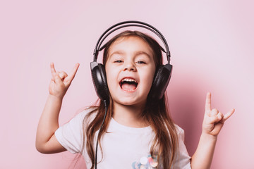 Cute little girl listening music wearing headphones on pink background. Funny emotions. Copyspace...