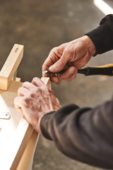Custom woodworking and carpentry. Close up of a carpenter's hands holding wooden plank and chisel