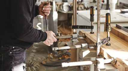 Cropped image of worker gluing the wooden structure. Joiner clamps. Wooden construction under the press. Wooden products to order.