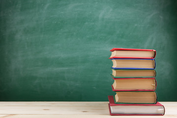 Education and reading concept - group of colorful books on the wooden table in the classroom, blackboard background