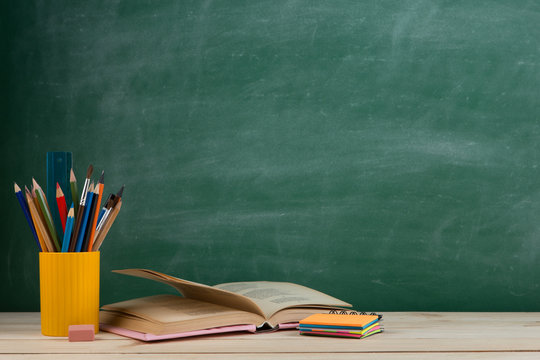 Education and reading concept - group of colorful books on the wooden table in the classroom, blackboard background