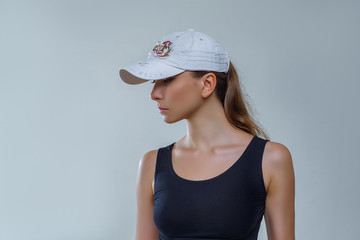 Beautiful woman in white baseball cap and black shirt posing stylishly in profile on gray background in studio. Fashion photography of accessories with sexy female model