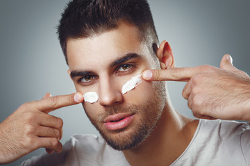 Close up of young man with moisturizer on the face in studio on gray background