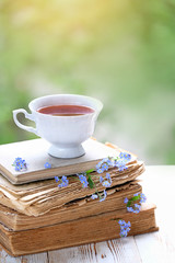 beautiful cozy composition with Cup of tea, blue flower and old books on wooden white table. spring, summer season. delicate home interior. 