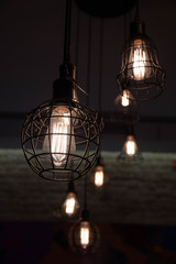 Lamps with filaments glowing inside glass light bulbs in darkness. Geometric lights shapes on dark background. Urban style interior lighting with wire cage lampshades. Industrial style lanterns