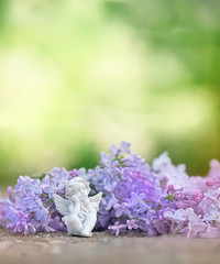 Beautiful angel and Spring lilac flowers in garden. White Cupid and lilac flowers on Beautiful Orchard green background. Springtime, romantic scene. concept for mothers day, valentine day. soft focus