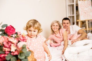 Obraz na płótnie Canvas beautiful family dad mom and daughter in pajamas having fun in the bedroom on the bed in a bright apartment