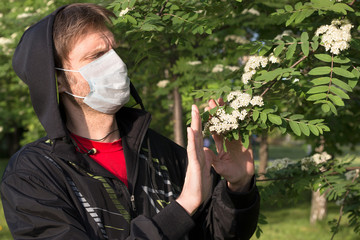 Man wearing a medical mask shows Stop gesture to a flowering branches. Seasonal allergic reaction to pollen. Stop to allergens