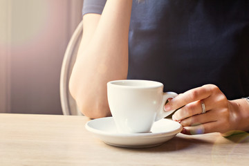 A cup of coffee in a cafe and a girl's hands.