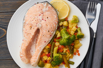 Steam salmon and vegetables, healthy diet. White plate on rustic wooden table, top view, close up