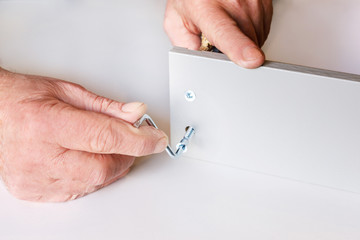 the process of screed two walls of the kitchen box when assembling furniture. One of the screws is already tightened, the second is tightened by male hands. Close-up