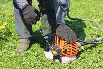 Close up hands in black work gloves of a gardener worker start motor of plant petrol lawnmower  -...