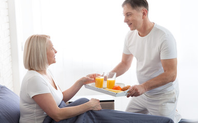 Attractive man holding breakfast tray to happy relaxed woman in bed