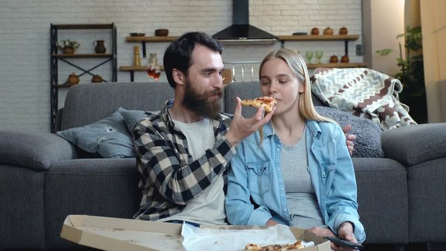 Young couple relaxing, watching TV and eating pizza at home.