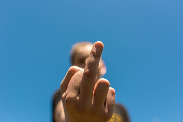Frustrated teenage boy showing the middle finger to the camera, beautiful blue sky background.