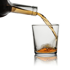 Whisky from a bottle is poured in a glass. Isolated on a white background with reflection