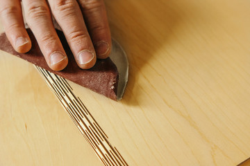 Hand sanding plywood with sandpaper. The process of polishing plywood after laser processing. Carpenter working. Sanding pink plywood detail with sandpaper