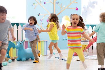 Group of happy children of boys and girls run in day care. Kids playing in kindergarten - obrazy, fototapety, plakaty