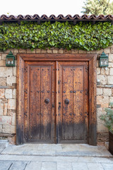 Big old fashioned antique wooden door surrounded with white stones and green leaves.