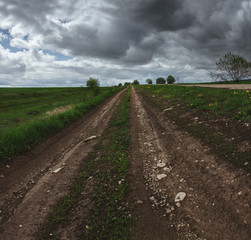 Fototapeta na wymiar Cloudy spring landscape with ground country road