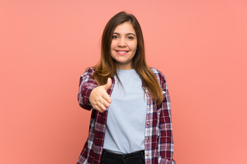 Young girl over pink wall shaking hands for closing a good deal