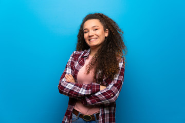 Teenager girl over blue wall keeping the arms crossed in frontal position