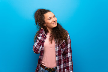 Teenager girl over blue wall thinking an idea while scratching head