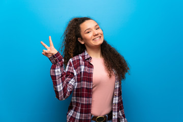 Teenager girl over blue wall smiling and showing victory sign