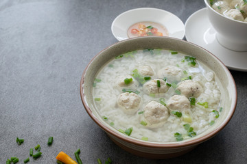 Rice soup with chicken ball and scallion in gray bowl on table.