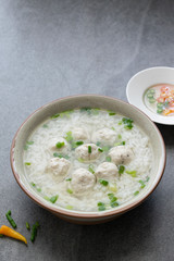 Rice soup with chicken ball and scallion in gray bowl on table.