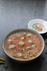 Rice spicy soup with chicken ball and chilli in gray bowl on table.
