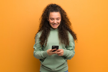 Teenager girl over ocher wall sending a message with the mobile