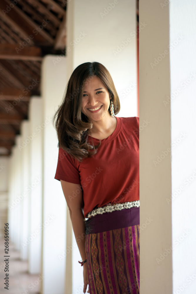 Wall mural Beautiful Asian woman by wearing sarong looking at camera on the blurred background of the pole buildings