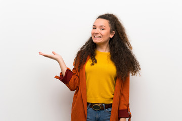 Teenager girl with coat holding copyspace imaginary on the palm to insert an ad