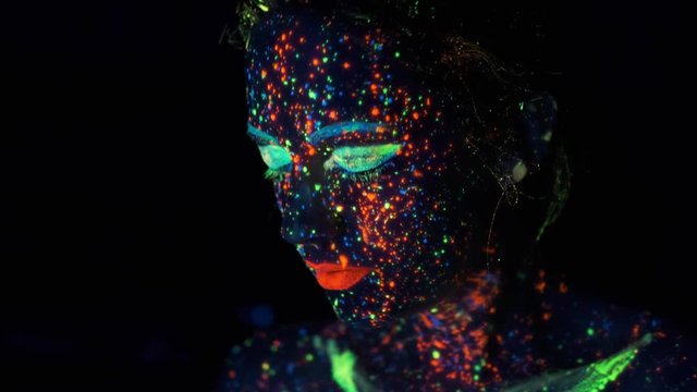 paint glowing in ultraviolet light. portrait of a girl colored with glowing paint.