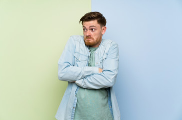 Redhead man over colorful background making doubts gesture while lifting the shoulders