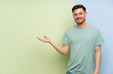 Redhead man over colorful background holding copyspace imaginary on the palm