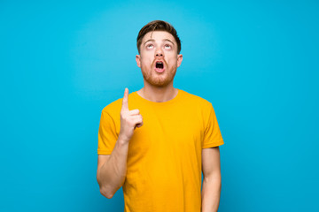 Redhead man over blue wall pointing up and surprised